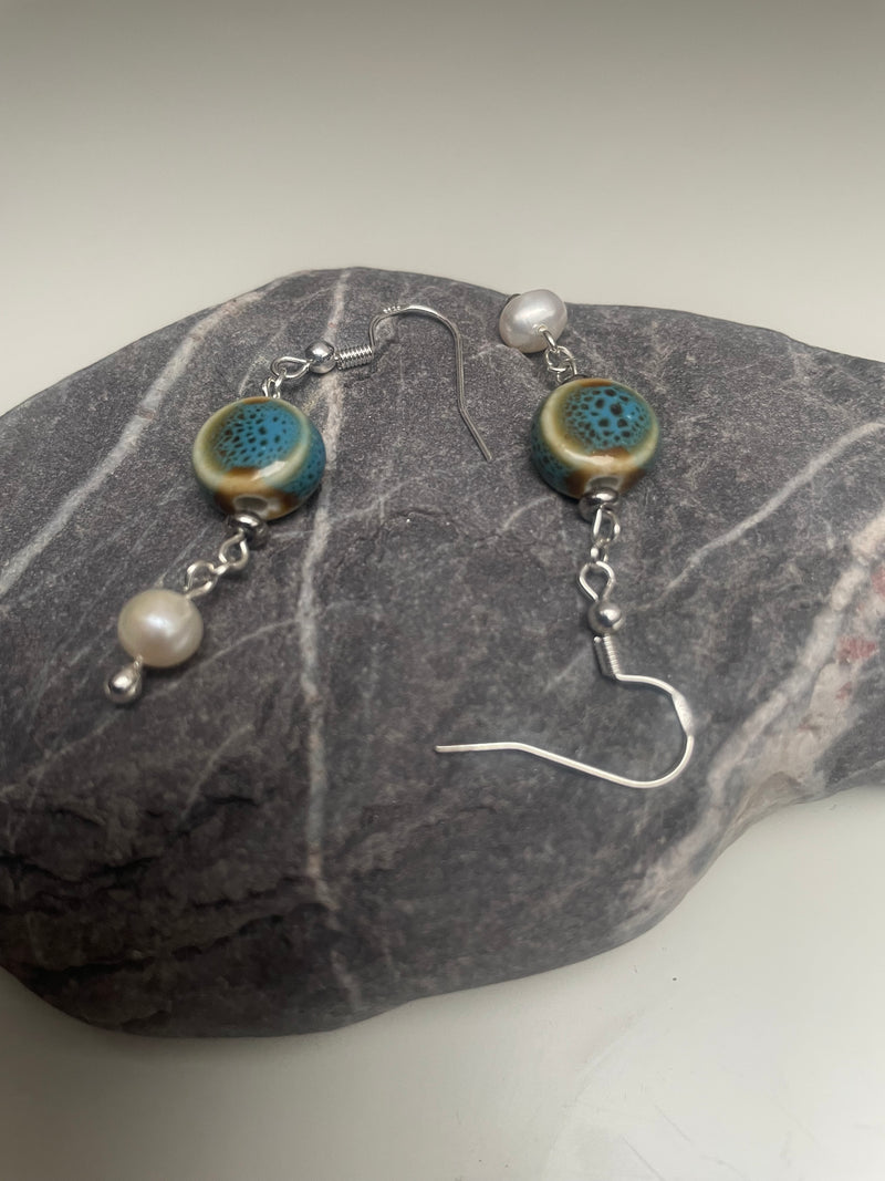 Close-up of MAYIA handmade blue ceramic and pearl earrings