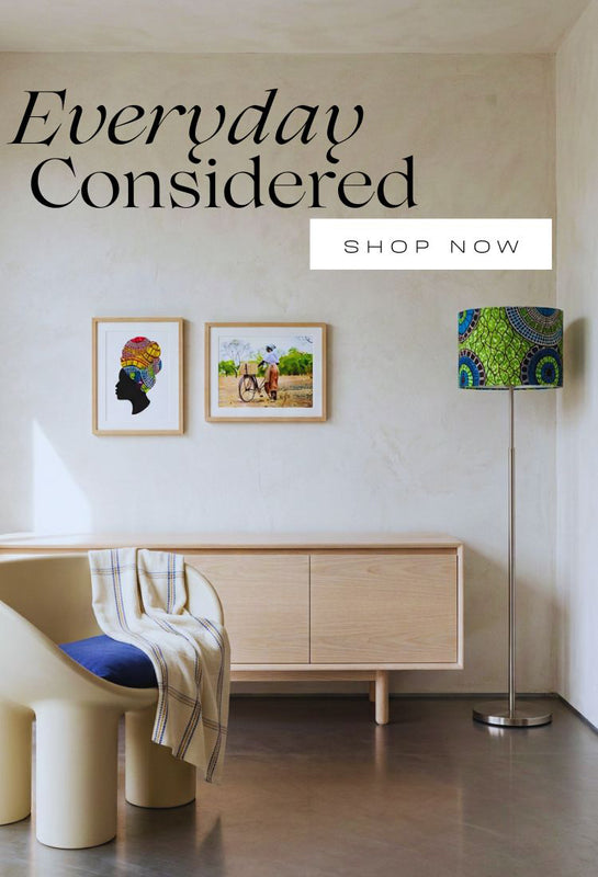 A styled interior scene with a cream chair draped with a striped throw, a light wood sideboard, a patterned Ollie floor lamp and two framed wall art pieces.  Large overlaid text reads 'Everyday Considered' with a 'SHOP NOW' banner.